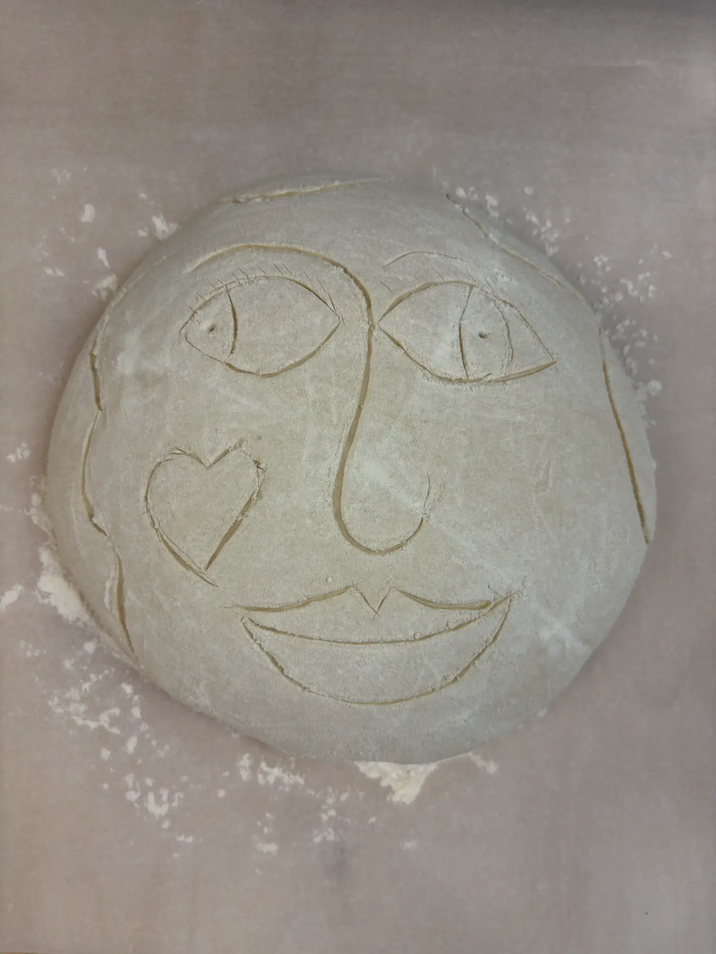 Sourdough loaf scored with a smiling face, draped in a grey cloth — alternate view
