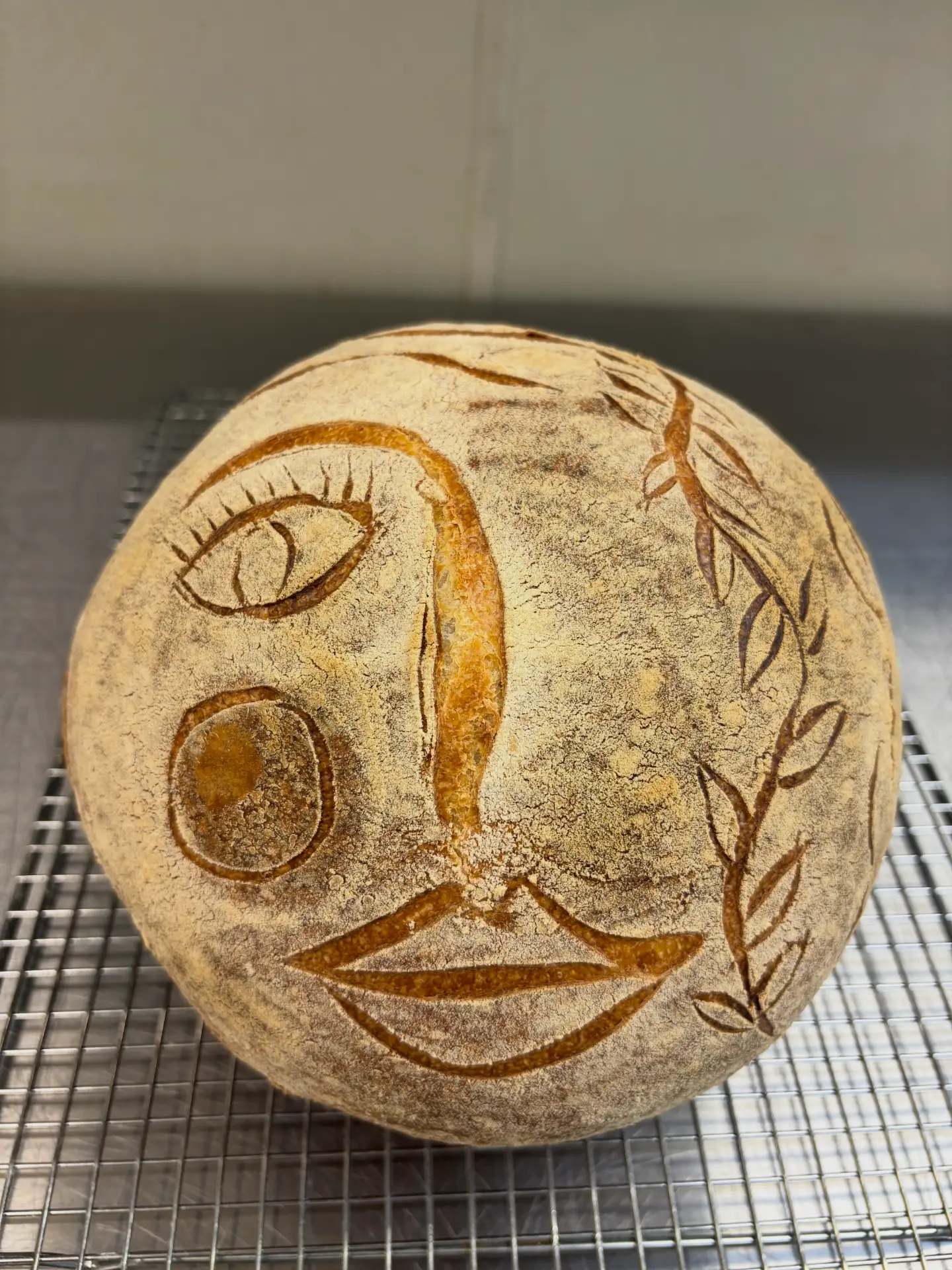 Sourdough loaf scored with a face and olive branch — alternate view